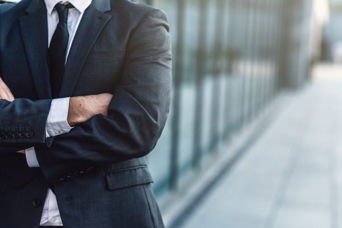 Businessman  crossing his hands posing on background of office building , blurred background.